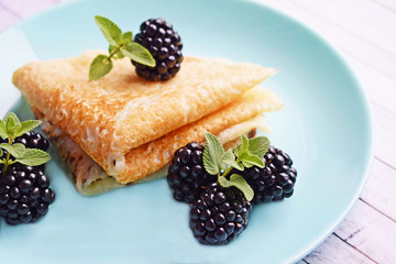 Delicious hot pancakes with blackberries and mint on a wooden background.