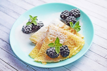Delicious hot pancakes with blackberries and mint on a wooden background.