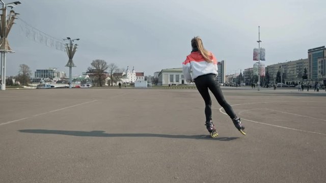 Back view of girl on roller skates. Attractive woman riding roller skating in street. Urban background