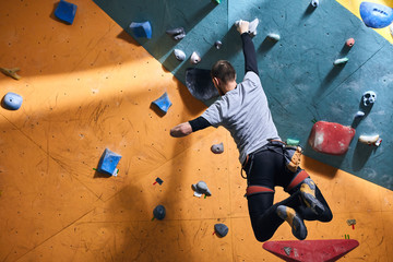 Unrecognizable powerful boulderer with physical disability hanging at climbing wall, balancing on...