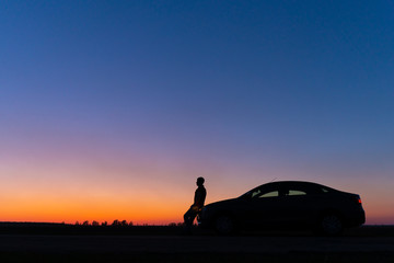 Silhouette of a man and a car on a background of a very beautiful sunset. Freedom and travel by car concept.