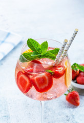 Pink gin and tonic cocktail with prosecco and strawberries, garnished with fresh mint - refreshing summer alcoholic drink