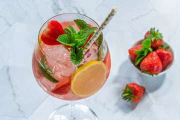 Pink gin and tonic cocktail with prosecco and strawberries, garnished with fresh mint - refreshing summer alcoholic drink