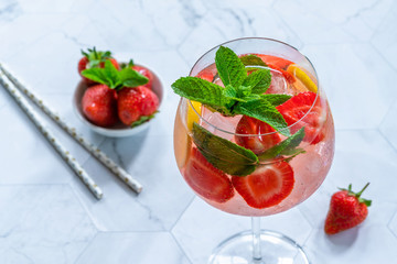 Pink gin and tonic cocktail with prosecco and strawberries, garnished with fresh mint - refreshing summer alcoholic drink