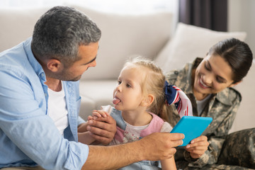 Funny daughter showing tongue to daddy while having fun with family