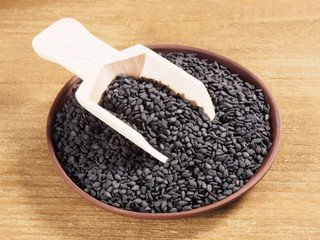 Black sesame (Sesamum indicum) in a clay plate with scoop on a wooden background