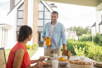Husband bringing some orange juice for breakfast with wife outside