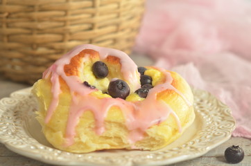 Bun with cheese and blueberries with icing on a rustic plate