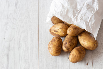 New potatoes in a white paper bag, environmentally friendly biodegradable packaging, with a grey wood background