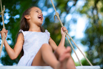 Happy girl rides on a swing in park. Little Princess has fun outdoor, summer nature outdoor....
