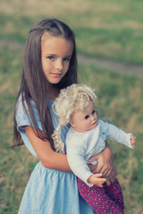 Pretty little girl posing  in blue dress with vintage doll, summer nature outdoor. Kid's portrait. Beautiful child's calm face