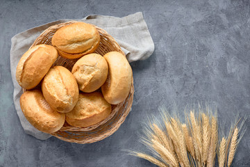 Bread buns in basket on rustic wood with wheat ears, top view on grey