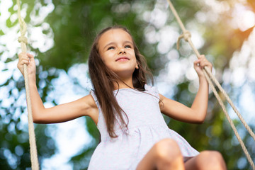 Happy girl rides on a swing in park. Little Princess has fun outdoor, summer nature outdoor....