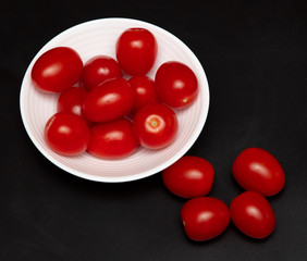 Red cherry tomatoes in a white plate on a black background
