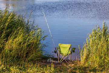 A fishing rod with a chair on the shore of a pond