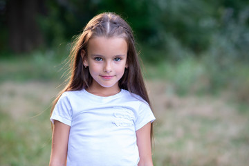 Pretty little girl with long brown hair posing summer nature outdoor. Kid's portrait. Beautiful child's face