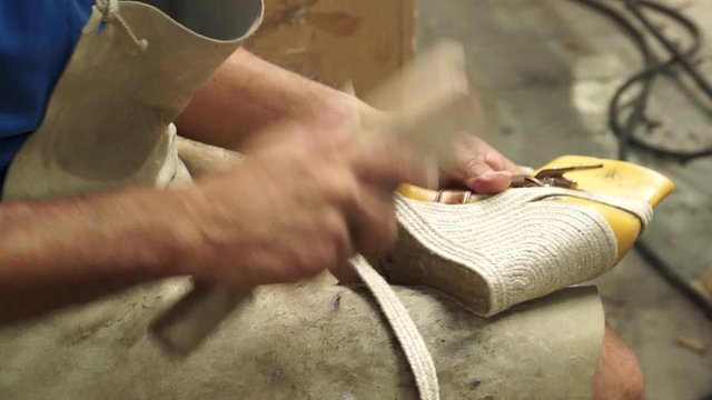 Static close-up shot of a shoemaker banging the sole of a handmade shoe to align the stitching in a shoe workshop factory