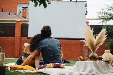 Couple in love watching a movie, during a picnic on the lawn in their courtyard.