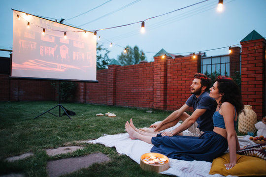 Couple In Love Watching A Movie, In Twilight, Outside On The Lawn In A Courtyard