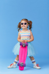 Stylish little toddler girl child in glasses with skateboard over blue background