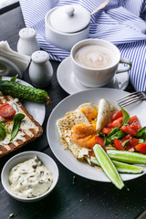 Tasty and healthy breakfast. Fried eggs, vegetable salad, toasts with cream cheese and arugula and cappuccino on a dark background. Vertical shot