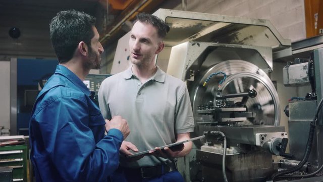 Two workers discussing a project in front of CNC lathe machine