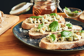 Close up on a plate of toasts with roquefort cheese, walnuts, honey and basil. Selective focus