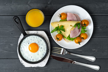 Breakfast of fried eggs in pan, toast with cheese, ham, lettuce, cherry tomatoes and orange juice. Delicious nutritious breakfast.