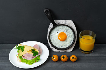 Breakfast of fried eggs in pan, toast with cheese, ham, lettuce, cherry tomatoes and orange juice. Delicious nutritious breakfast.