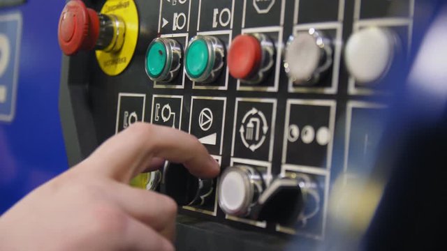 worker presses button on control panel in workshop closeup