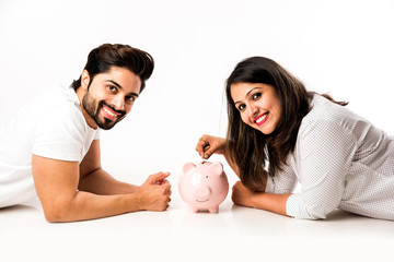 Indian couple with piggy bank lying over white background, side view