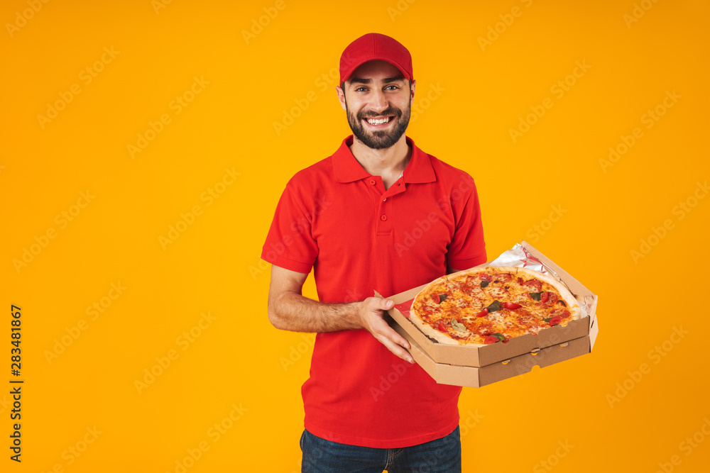 Poster photo of happy delivery man in red uniform smiling and holding pizza box