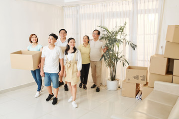 Fototapeta premium Cheerful Asian family entering new house. Cardboard boxes with their belongings standing in a corner