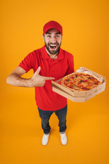 Full length image of attractive delivery man in red uniform smiling and holding pizza box