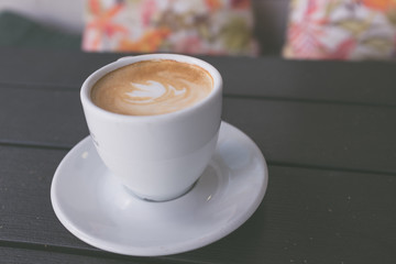 Cup of coffee on wooden table with colorful cushions in the background, vintage style