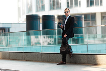 Handsome man with bag and phone outdoors.