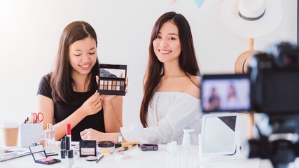 Two beautiful asian woman blogger showing how to make up and use cosmetics. In front of the camera...