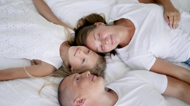 family with two children lie on a white big bed