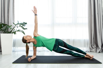 Young sporty woman standing in plank position at home
