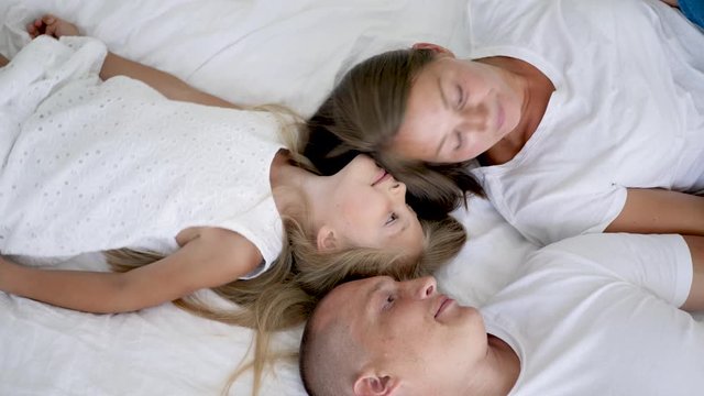 family with two children lie on a white big bed