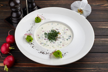 Okroshka in a white plate on a wooden table