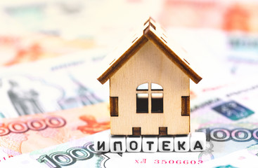 finance concept in blocks with word Mortgage (in Rissian language) and wooden symbol house on the stack of Russain rubles