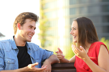 Happy couple talking sitting on a bench in the street