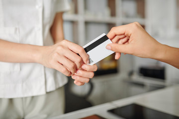Hands of young woman giving credit card to receptionist to pay for precedure