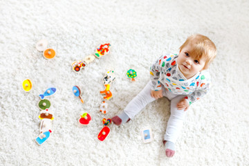 Fototapeta na wymiar Gorgeous cute beautiful little baby girl playing with educational toys like wooden puzzle at home or nursery. Happy healthy child having fun with colorful different toys. Kid learning different skills