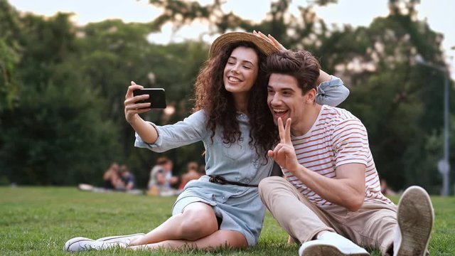 Happy romantic couple sitting on grass and take a selfie by mobile phone