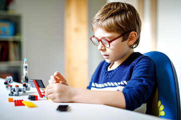 Little blond child with eye glasses playing with lots of colorful plastic blocks. Adorable school kid boy having fun with building and creating robot. Creative leisure modern technic and robotic.