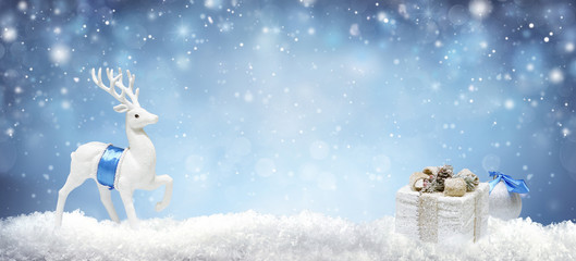 Christmas background with white decorative deer and gift box in snow on evening blue sky background...
