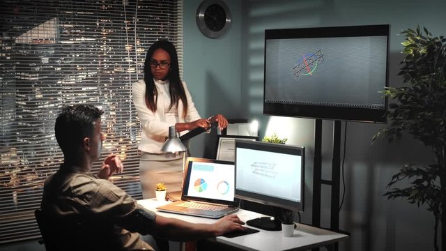 Male architect working in 3D software speaking with project enginner about bridge truss model seen on big screen and computer monitor