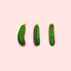 Flat lay composition with 3 fresh cucumbers on a pink background.